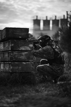 Soldier in combat gear crouched beside stacked ammunition boxes in monochrome.