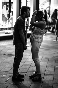 Two people facing each other in conversation on a pedestrian walkway at night.