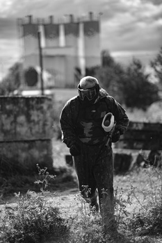 Motorcyclist in leather jacket riding dirt bike through overgrown field with stone tower in background.