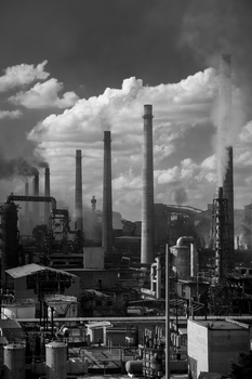 Industrial factory complex with multiple tall smokestacks against a dramatic cloudy sky.