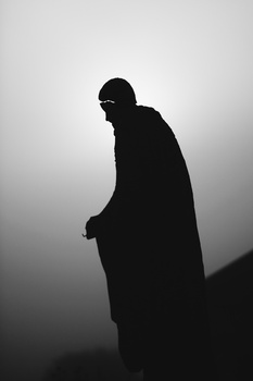 Silhouetted figure in dramatic backlit pose against gray gradient background.