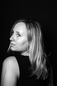 Woman with long straight hair in profile against a black background, wearing a sleeveless black top.