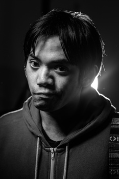 Black and white portrait of a person in a hoodie lit with dramatic side lighting against a dark background.