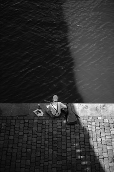Overhead view of a person sitting alone on a wet tiled surface with a sharp shadow cast across the frame.