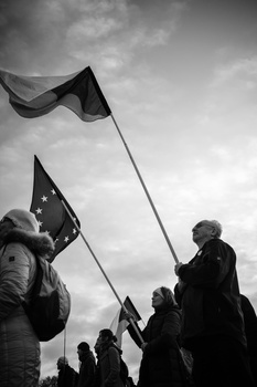 Group of people holding flags aloft during an outdoor gathering, photographed in black and white against a cloudy sky.