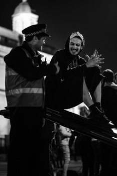 Two people on a film set at night, one wearing a safety vest and hat, the other gesturing while speaking.