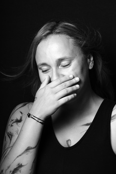 Woman with eyes closed, hand covering lower face, against dark background in studio portrait.