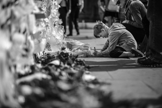 Person sitting on pavement with flowers in shallow focus foreground, black and white photograph.