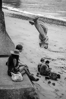 Black and white photograph of children playing on a beach near water and concrete structure.
