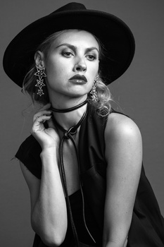 Woman wearing a wide-brimmed black hat and dangling earrings, posed against a neutral background in black and white.