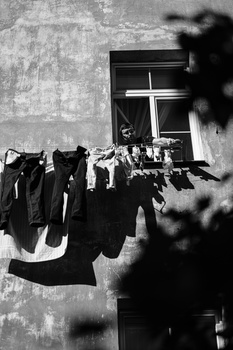 Black and white photograph of laundry hanging on a clothesline against a weathered building facade with a window.