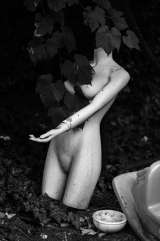 Kneeling figure in monochrome, partially obscured by foliage, with arm extended downward.