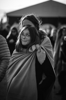 Woman wearing glasses and wrapped in fabric at an outdoor event, captured in black and white.