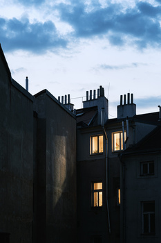 Silhouetted residential building with warm-lit windows against twilight sky with clouds.
