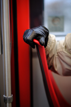 Hand in black glove gripping a bright red rope or strap against blurred background.