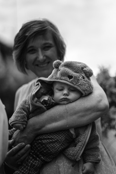 Woman holding a young child wearing a knit hat, both smiling at camera in black and white.