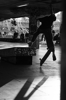 Skateboarder mid-trick airborne in concrete skate park beneath covered area.