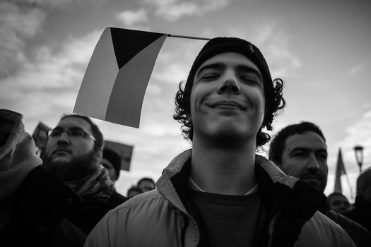 Man with curly hair smiling upward at a public gathering, photographed in black and white.