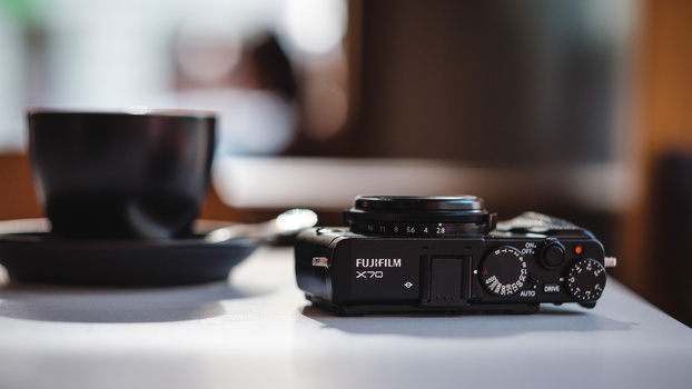Black Fujifilm X-Pro camera displayed on a white surface with accessories in soft, warm studio lighting.