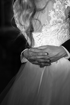 Bride's hands holding a bouquet, wearing an ornate lace wedding dress in black and white.