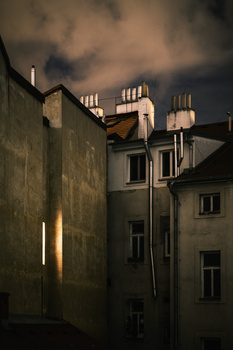 Nighttime architectural photograph of urban buildings with dramatic stormy sky and warm artificial lighting.