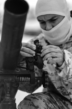Person in winter clothing aiming a rifle with optical scope attachment.