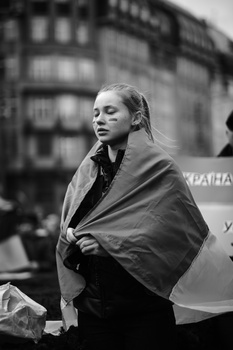 Woman wearing a draped shawl in a urban street setting, photographed in black and white.
