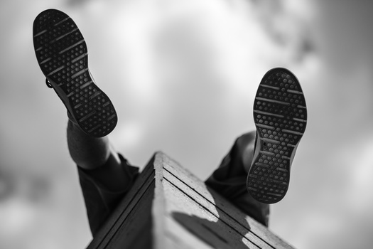 Upward view of two feet in dark shoes with soles visible against a cloudy sky.
