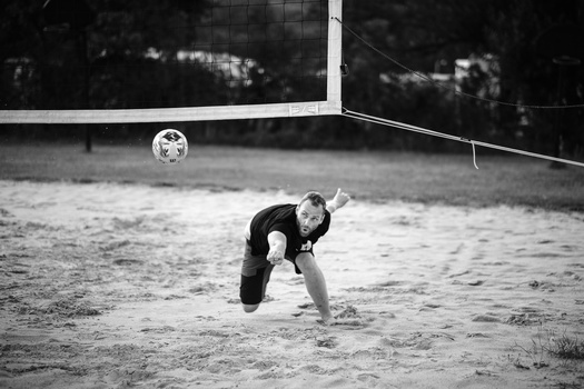 Beach volleyball player diving to save the ball during a sandy court match in black and white.
