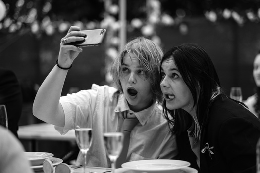 Two people taking a selfie at a dining table, both with surprised expressions.