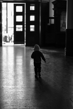 Young child walking alone across a wet concrete floor in a minimalist interior space.