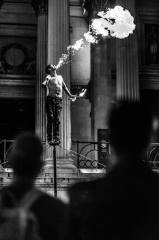 Skeleton statue exhales a large cloud of smoke against classical columns in black and white.