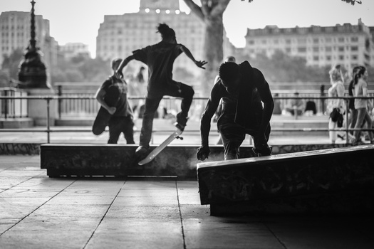 Skateboarder performing a trick on a ledge while others watch in an urban plaza.