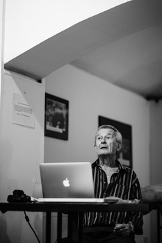 Black and white portrait of an older man looking upward while sitting at a desk with a laptop.