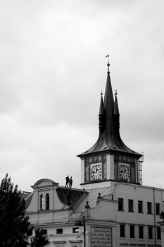 Black and white photograph of a clock tower with a pointed spire against an overcast sky.