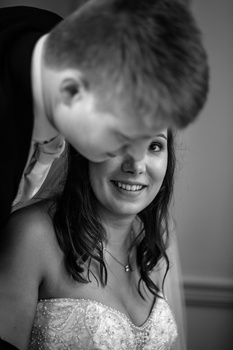 Woman smiling at camera while child leans playfully over her shoulder in black and white portrait.