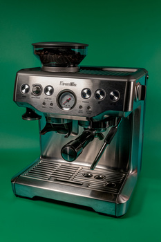 Breville espresso machine with grinder, portafilter, and steam wand against green background.