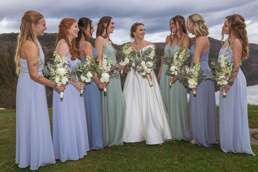 Bride and seven bridesmaids standing together outdoors holding white flower bouquets.