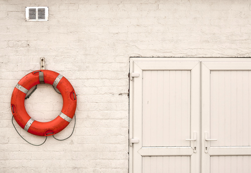 Red life preserver mounted on a white painted brick wall next to closed white doors.