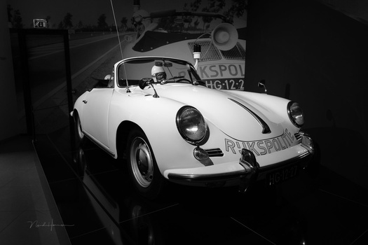 White convertible sports car displayed in a museum setting, photographed in black and white.