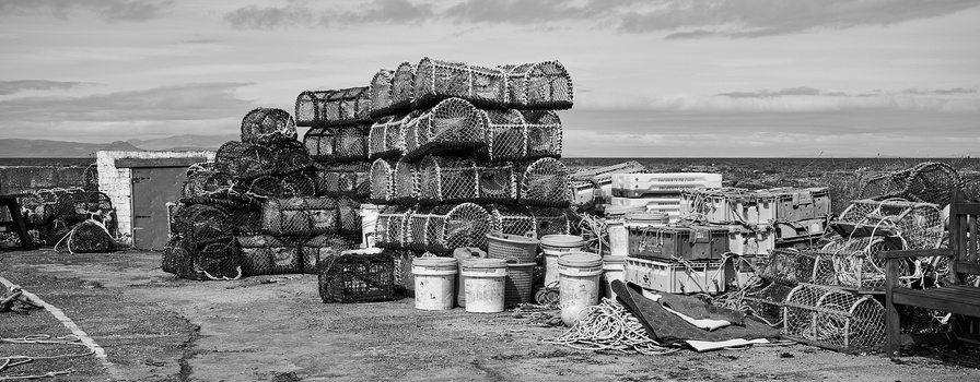 Stacked fishing crab and lobster traps with buckets and rope on a weathered dock.