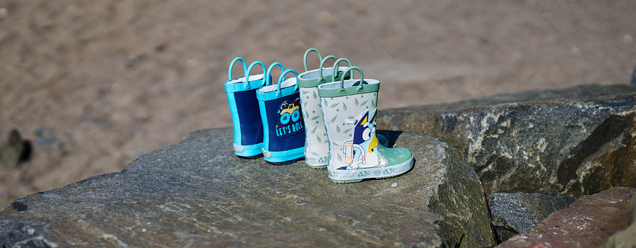 Four colorful children's boots and buckets arranged in a row on weathered stone.
