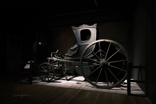 Antique horse-drawn carriage with large spoked wheels photographed under dramatic spotlight lighting.