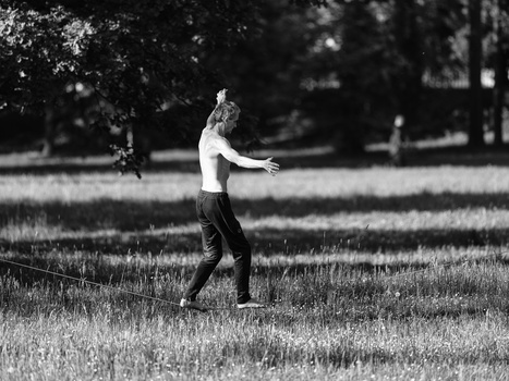 Shirtless young man running through an open grassy field with trees in the background.