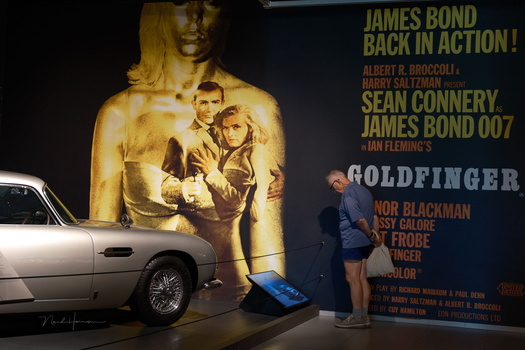 Classic Aston Martin DB5 displayed alongside a vintage James Bond film poster featuring Sean Connery.