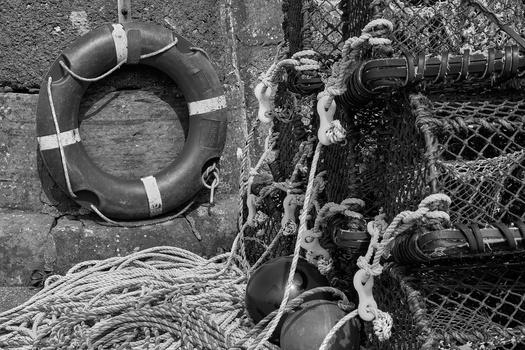Black and white photograph of weathered fishing equipment including a buoy, coiled rope, and lobster traps covered in frost or ice.