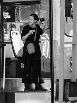 Black and white photograph of a woman in dark clothing standing in a doorway, looking to the side.
