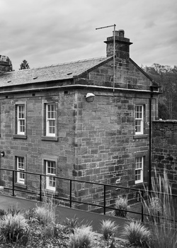 Black and white photograph of a two-story stone building with a chimney and windows.