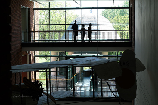 Silhouetted figures on a modern building balcony with expansive windows overlooking green landscape.