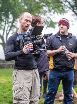 Cinematographer operating a professional video camera on set with crew members assisting outdoors.